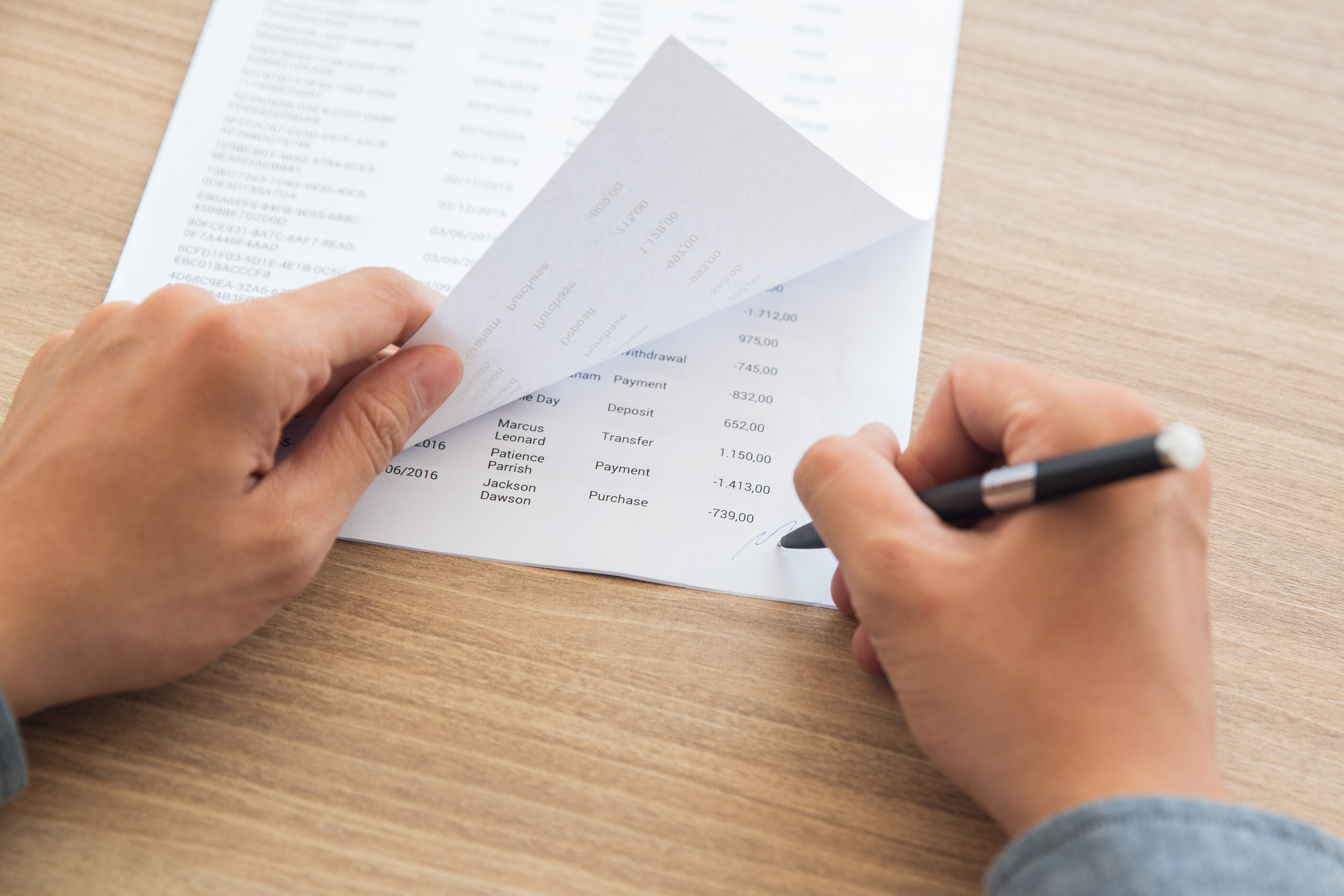 Close-up of male hands signing accounting documents. Businessman sitting at table in office